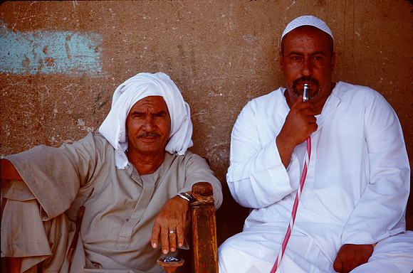 Two men sit in shade to smoke their hukkah.