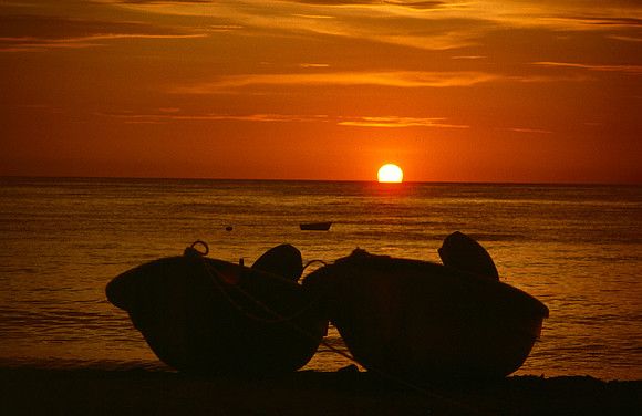 Silhouette of two boats on beach.