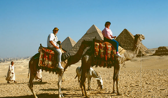 Two tourist on camels at the pyramids.